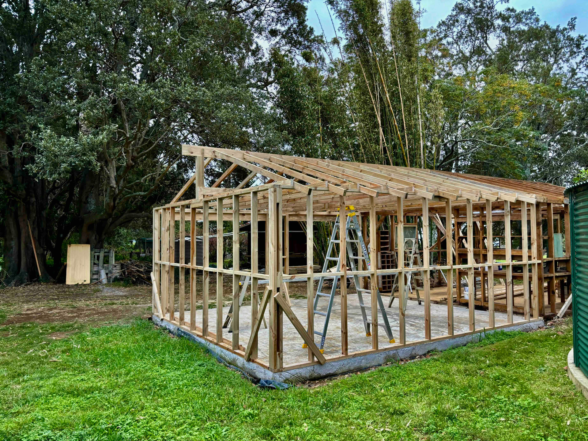 Timber-framed garden studio under construction on a concrete slab surrounded by trees