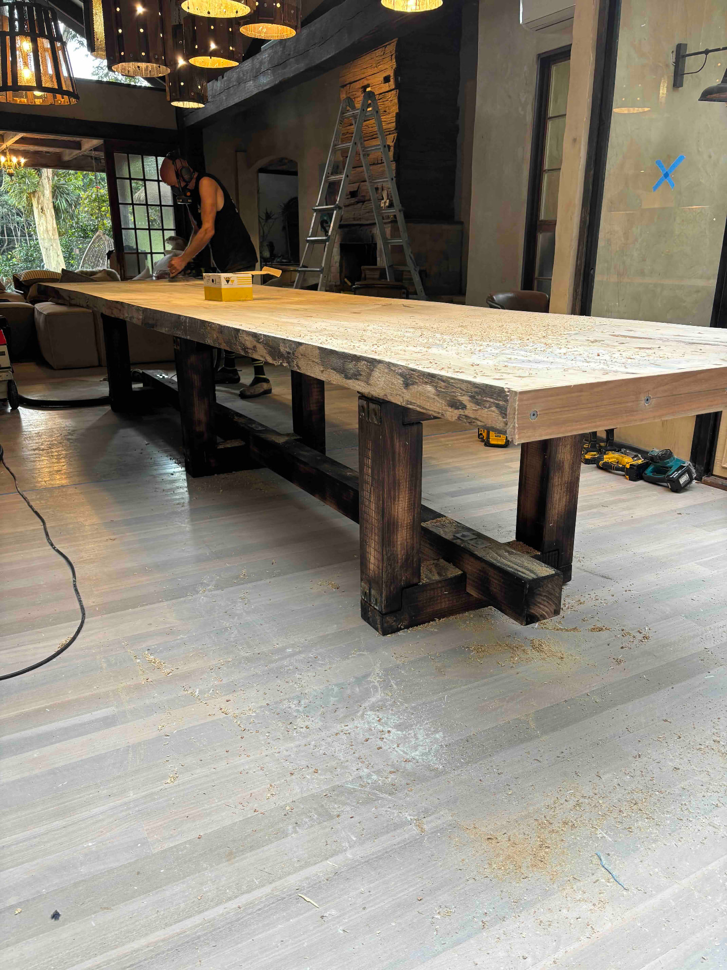 Long hardwood slab dining table with dark recycled timber legs being sanded on site