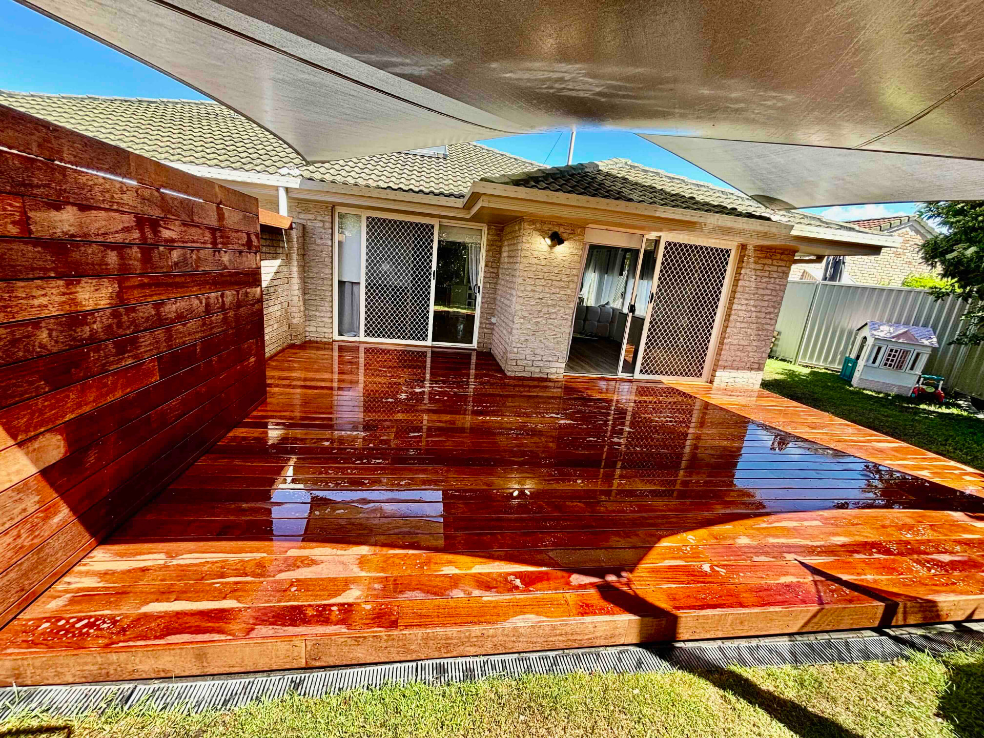 Low-level hardwood deck with a horizontal timber privacy screen under shade sails