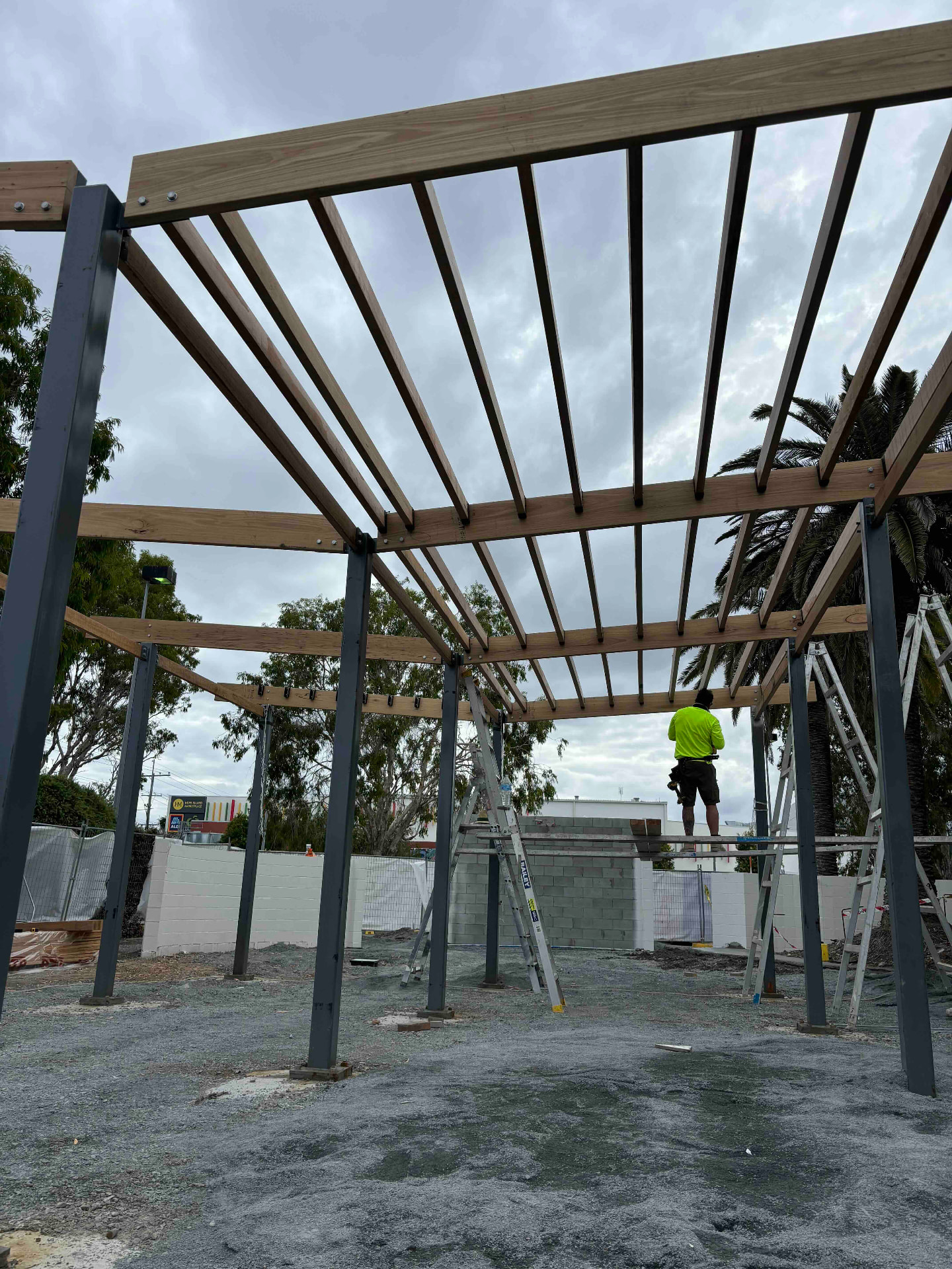 Large timber pergola rafters fixed to steel posts on a commercial building site