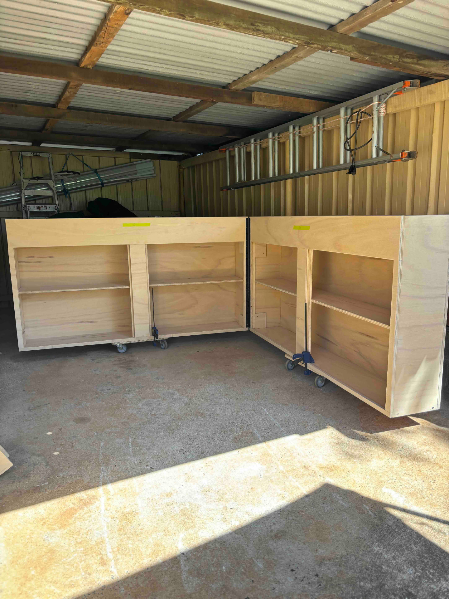Two plywood cabinet carcasses with shelving built on castors in a workshop