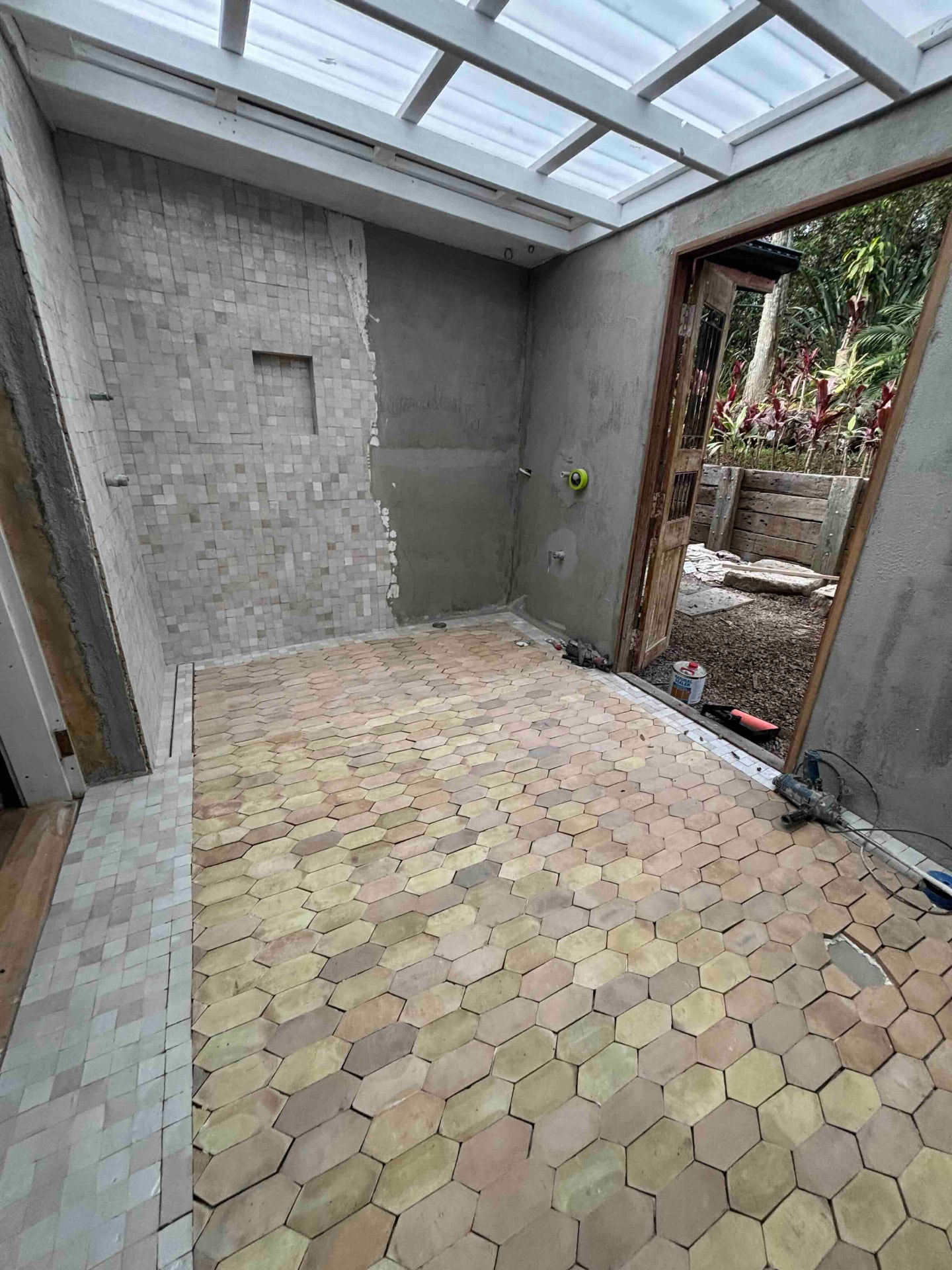 Outdoor bathroom under a skylight roof with hexagonal tiled floor and timber door frame